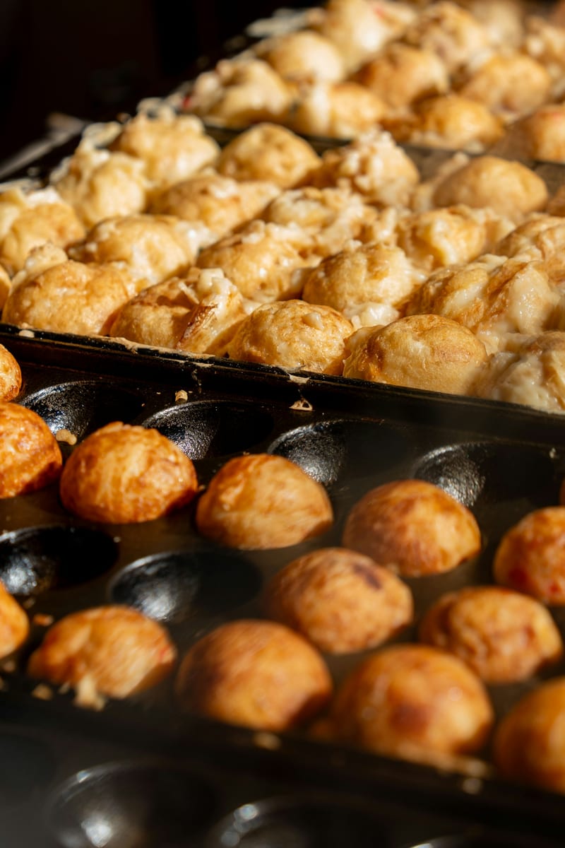 Takoyaki cooking in rows on a hot moulded pan