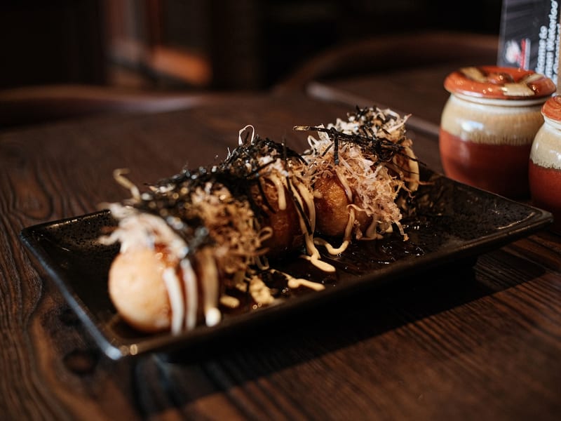 A plate of takoyaki finished with sauce and toppings